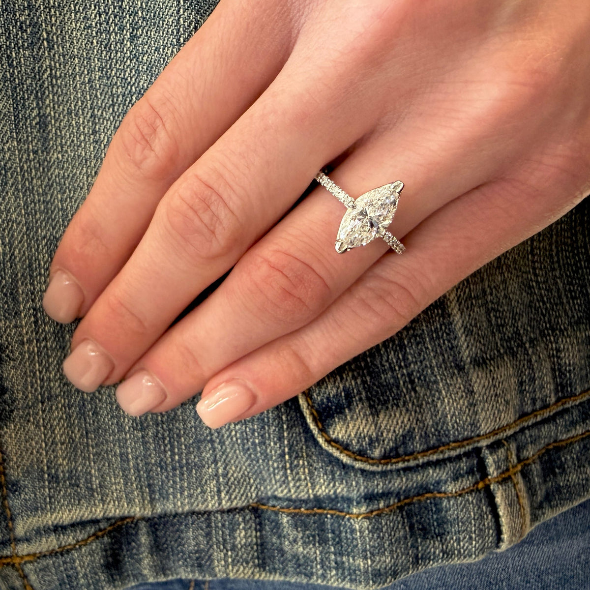 Hand wearing a diamond ring with denim background