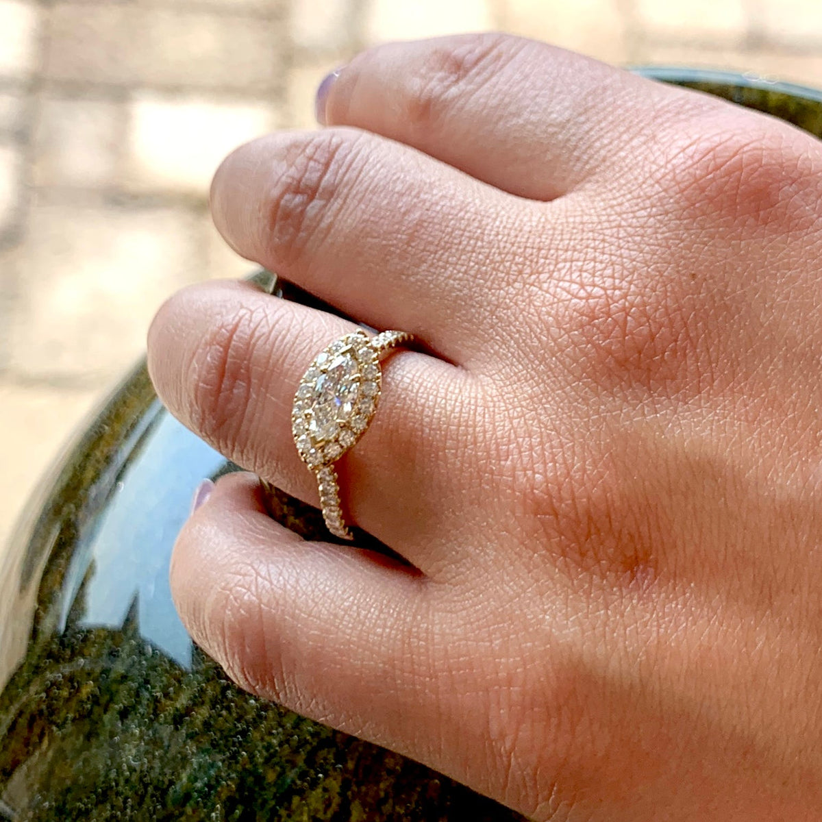 Close-up of a hand wearing a diamond ring with a blurred natural background