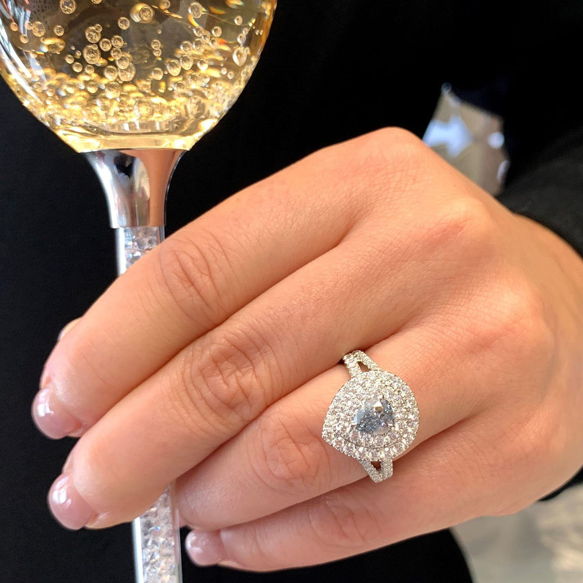 Hand holding a glass of champagne with a diamond ring on a black background