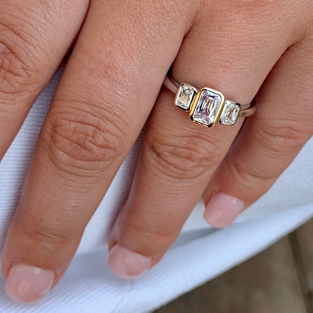 Close-up of a hand wearing a gold ring with emerald-cut gemstones on a white fabric background.