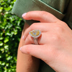 Hand wearing a yellow gemstone ring with a green background