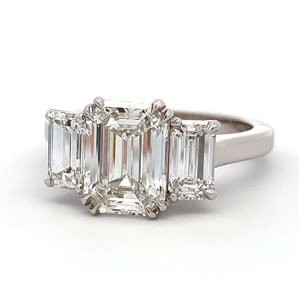 Diamond ring with emerald-cut center stone and baguette side stones on a white background