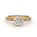 Gold ring with a large diamond and smaller diamonds on the band against a white background