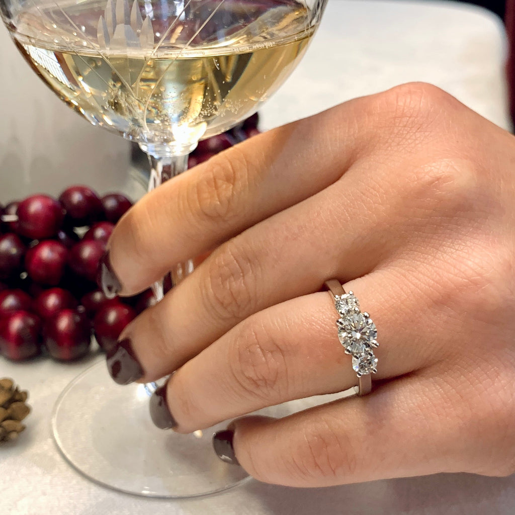 Hand wearing a diamond ring with a glass of white wine and grapes in the background