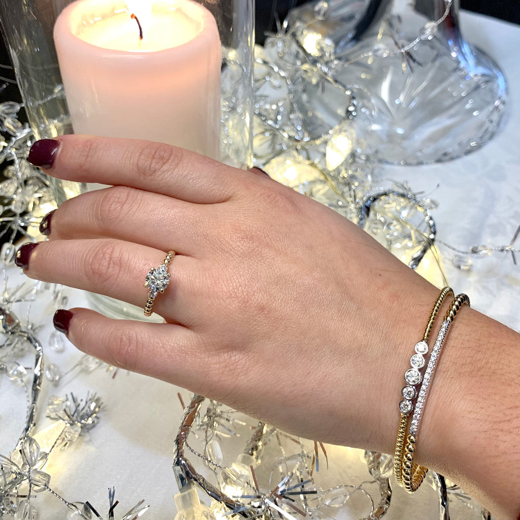 Hand wearing a ring and bracelets with a candle and decorative lights in the background
