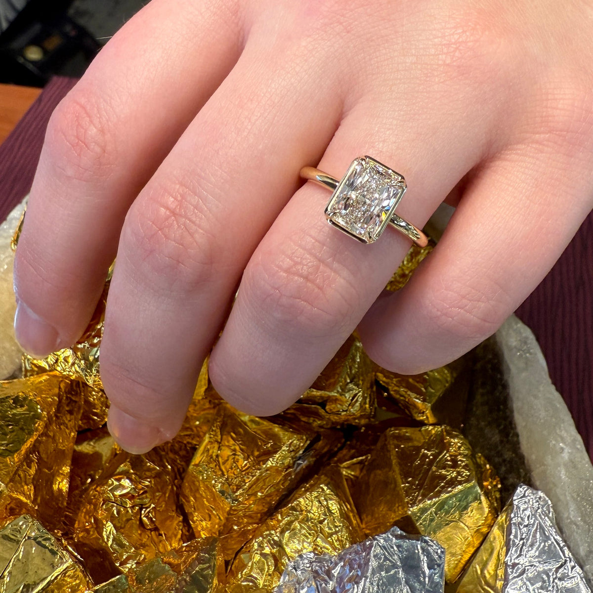 Hand wearing a diamond ring with gold leaf in the background