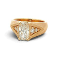 A yellow gold ring featuring a large rectangular radiant-cut diamond center stone, accented by smaller round diamonds on either side, set against a plain white background.