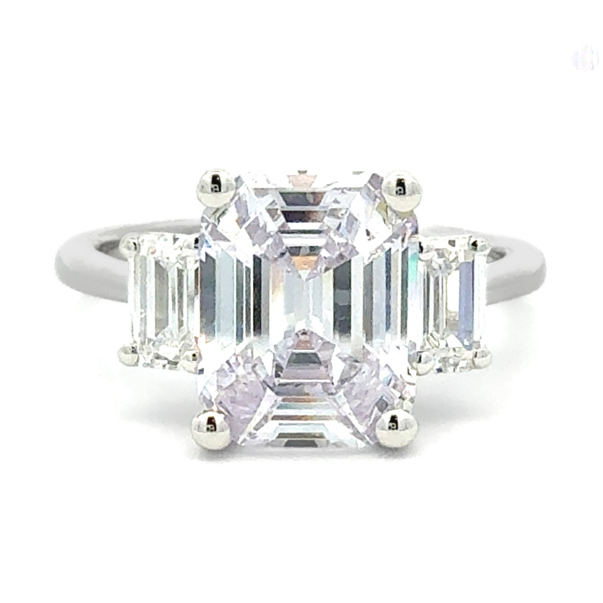 A three-stone diamond ring featuring a large emerald-cut center stone flanked by two smaller baguette-cut side stones, set in a silver-colored metal band on a white background.