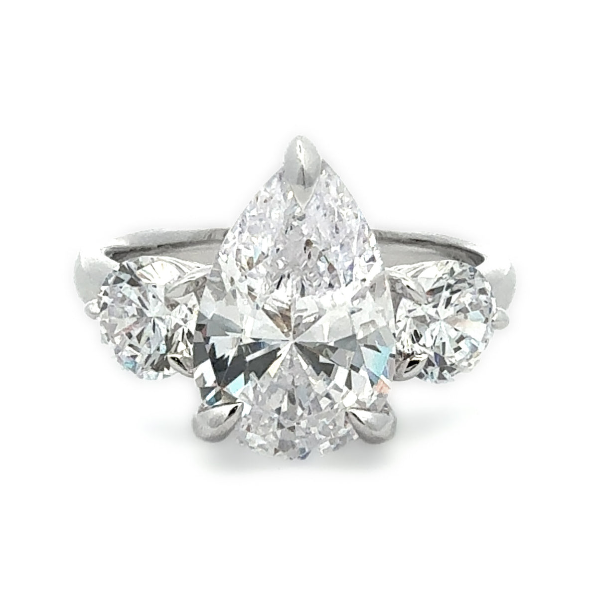 A three-stone diamond ring featuring a large pear-cut center diamond flanked by two round-cut diamonds, set in a silver-colored metal band on a white background.