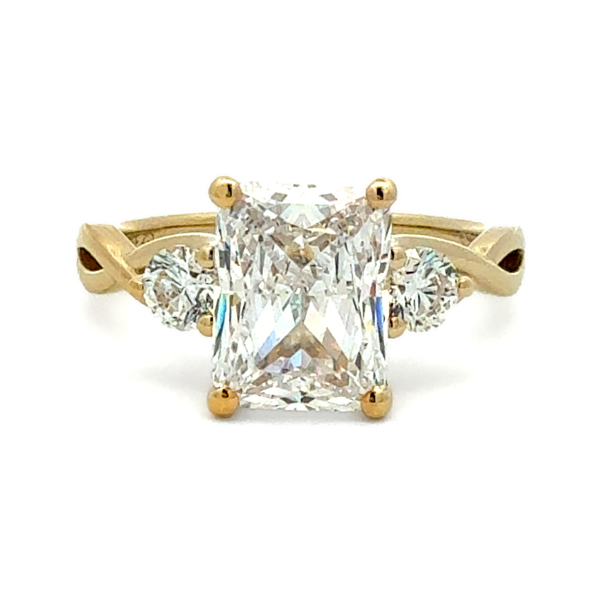 A yellow gold ring featuring a large rectangular princess-cut diamond center stone with two smaller round diamonds on either side of the band, set against a plain white background.