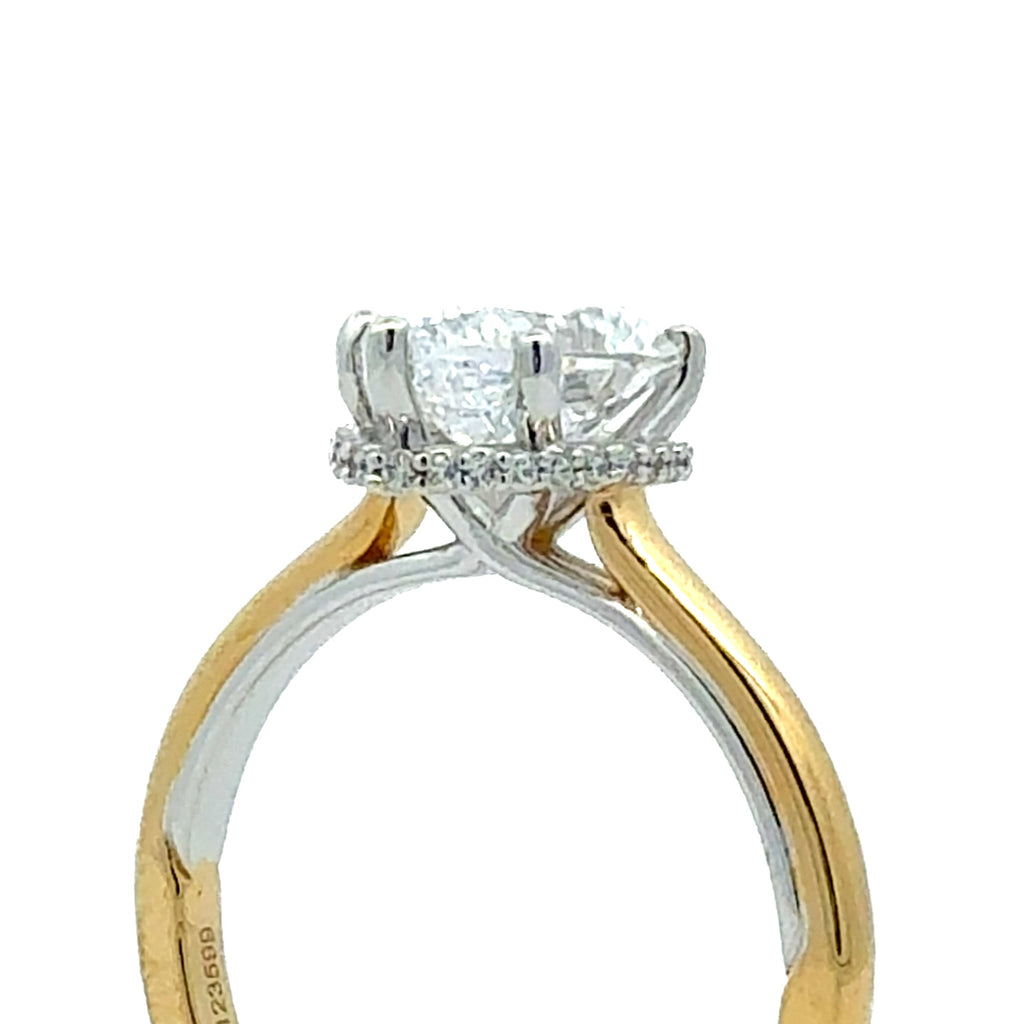 A close-up of a two-tone diamond ring featuring a yellow gold and white gold band with a brilliant round-cut center stone and a halo of small diamonds, set against a plain white background.
