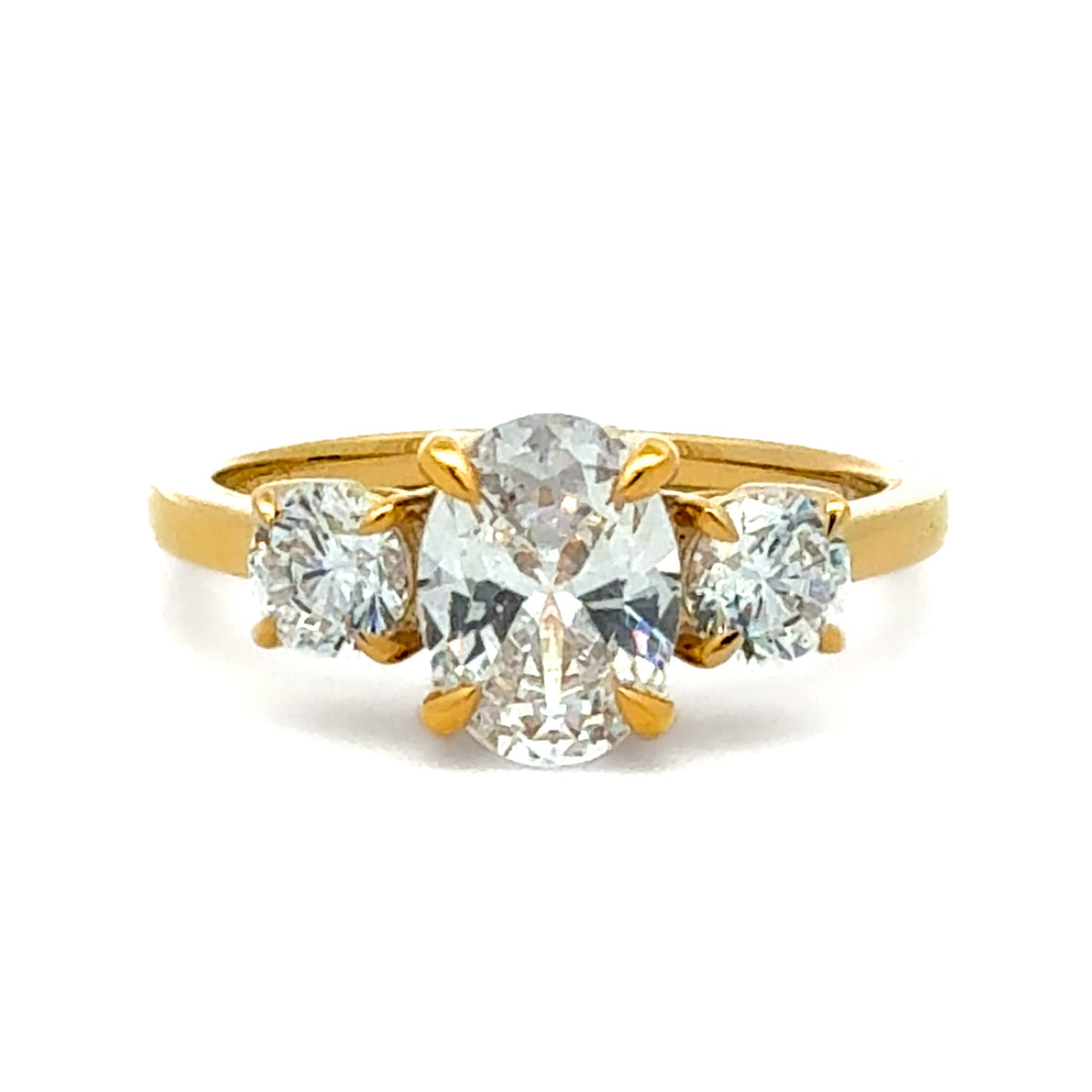 A yellow gold ring featuring a central oval-cut clear gemstone flanked by two round-cut clear gemstones on a white background.