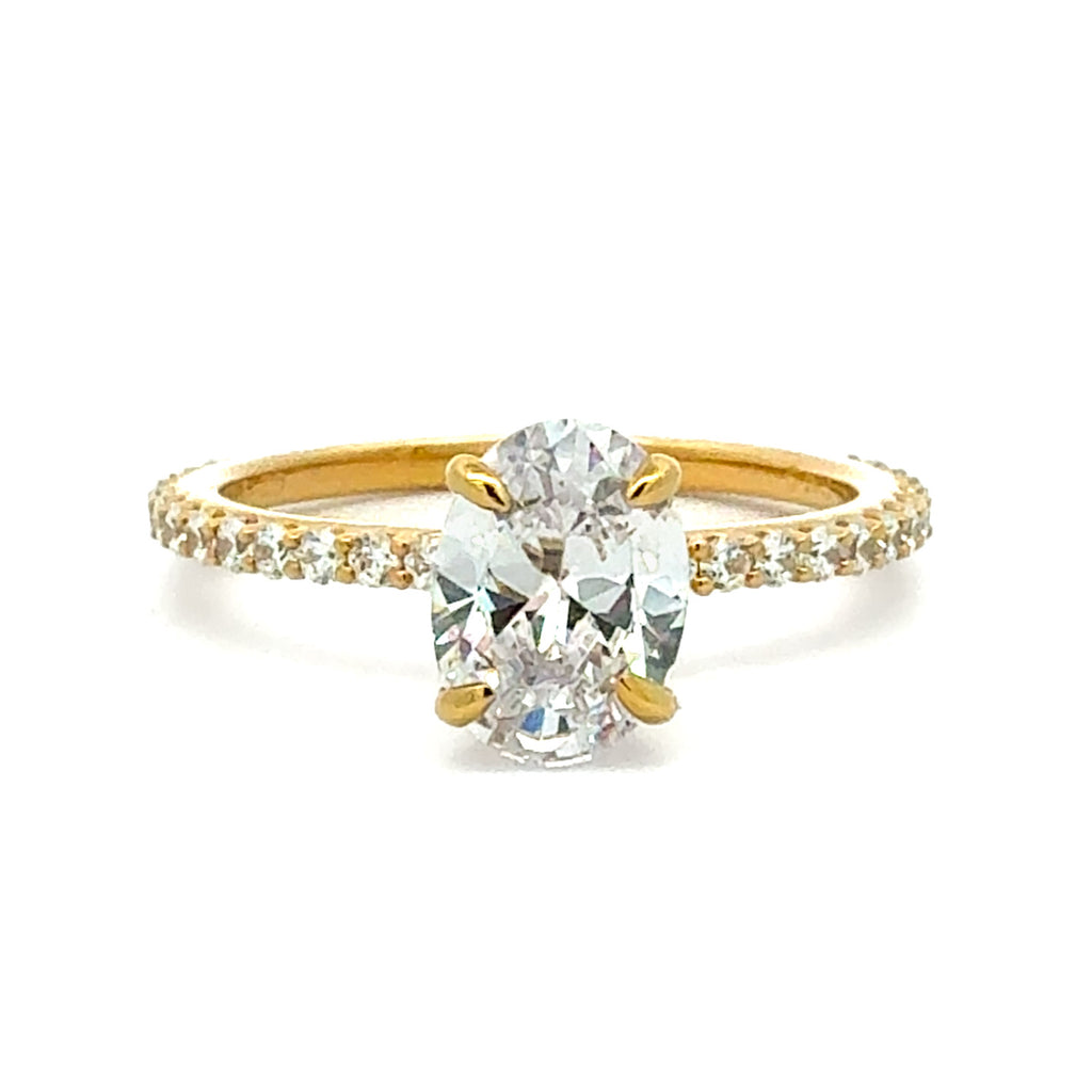 A yellow gold engagement ring featuring a large oval-cut center stone in a four-prong setting, with a pavé band accented by small round stones, shown on a plain white background.