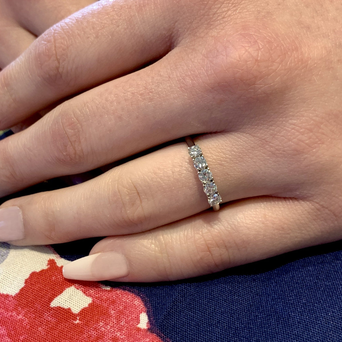 Close-up of a hand wearing a diamond ring on a floral fabric background