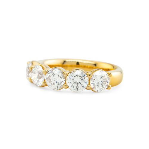 A yellow gold eternity ring featuring five round brilliant-cut diamonds set in a row, shown on a clean white background.