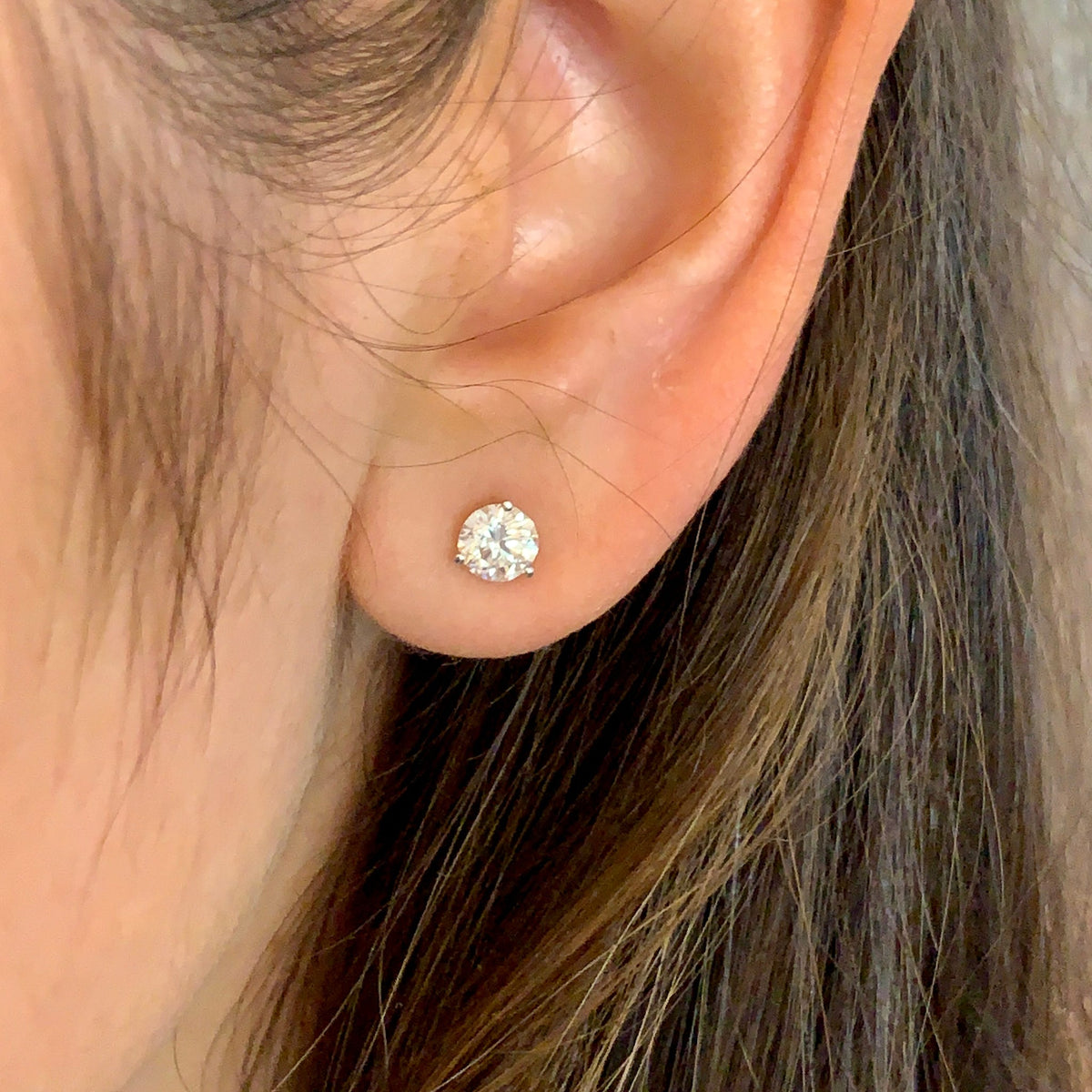 Close-up of an ear wearing a diamond stud earring with hair partially covering the frame.