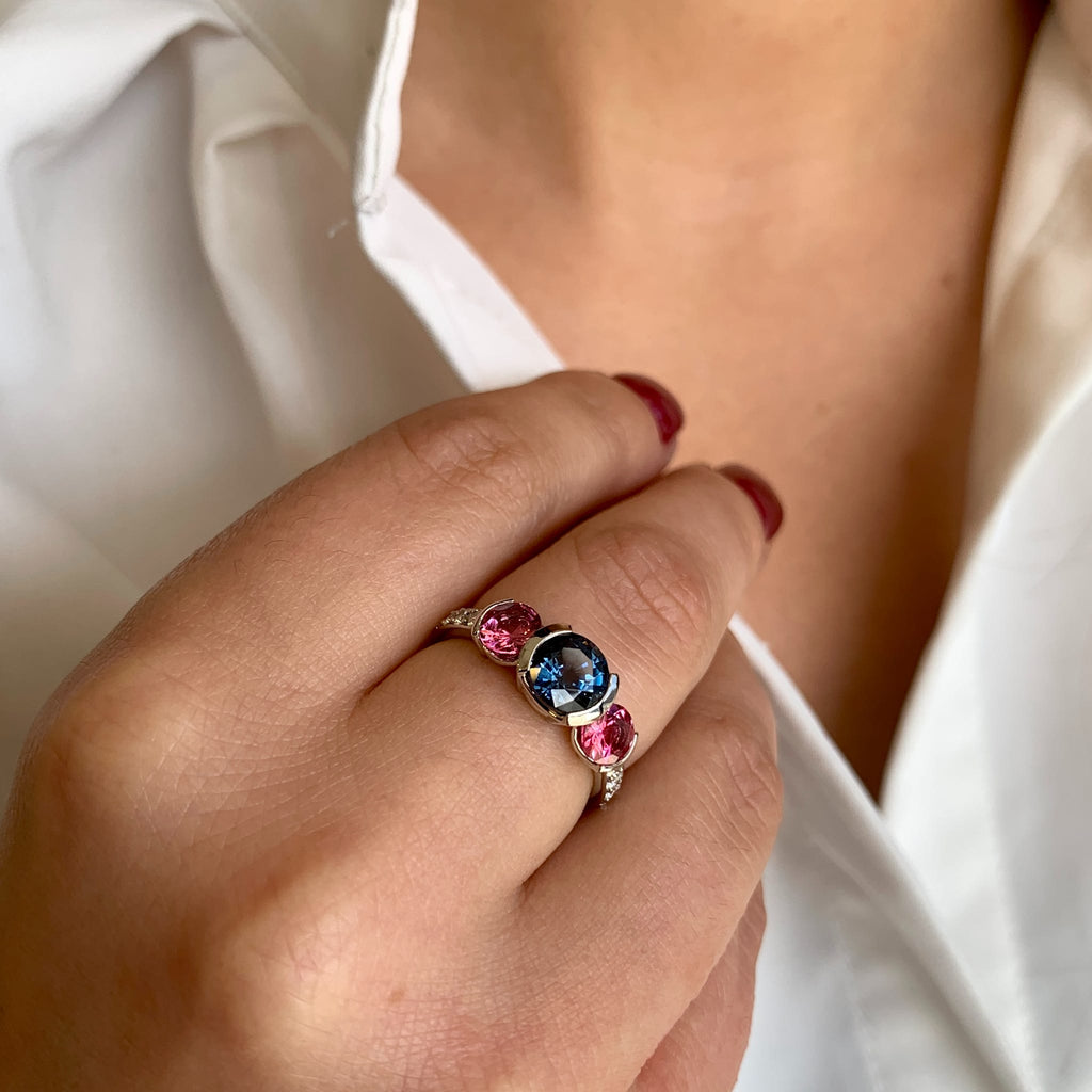 Close-up of a hand wearing a ring with a colorful gemstone against a white background