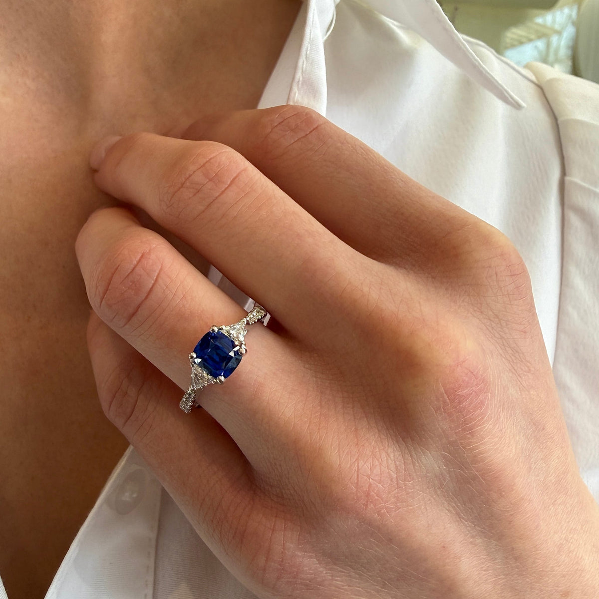 Close-up of a hand wearing a ring with a blue gemstone against a white shirt background