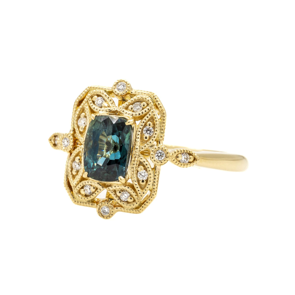 A yellow gold ring featuring a rectangular cushion-cut dark blue gemstone surrounded by an ornate filigree setting with small clear accent stones, shown on a plain white background.