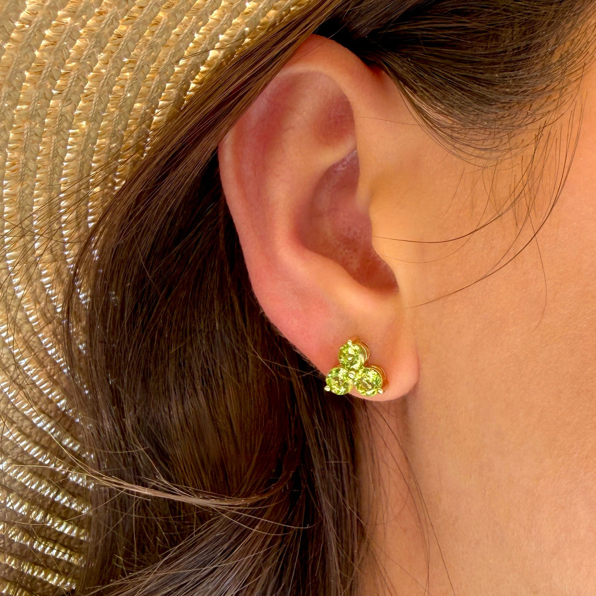 Close-up of an ear wearing a green earring with a straw hat in the background