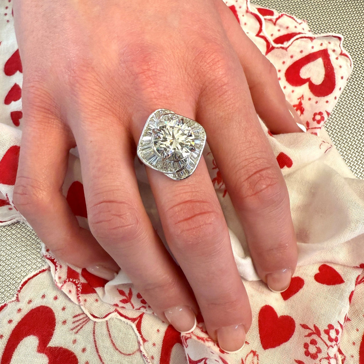 Hand wearing a diamond ring on a heart-patterned fabric background