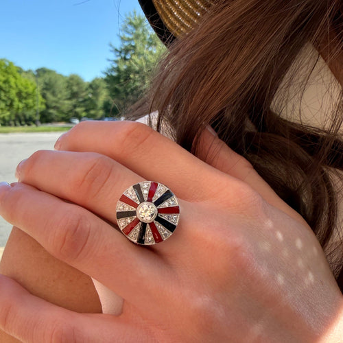 Close-up of a hand wearing a decorative ring with a colorful design outdoors.