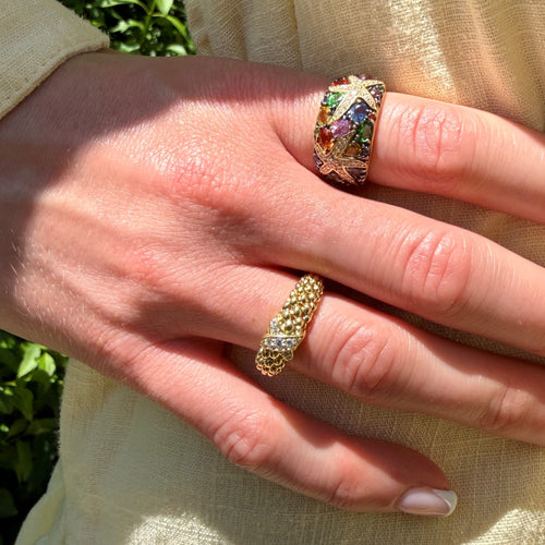 Close-up of a hand wearing two rings with a colorful gemstone ring on a light background