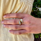 Hand wearing two gold rings with diamond accents on a beige fabric background