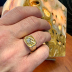 Hand wearing a gold ring with a diamond, holding a textured gold object.