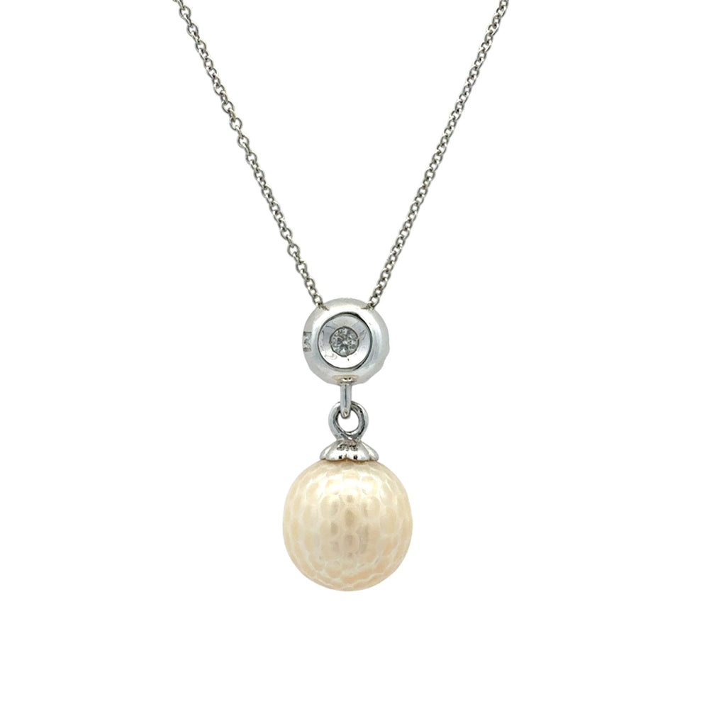 A silver chain necklace featuring a circular silver pendant with a small clear stone, from which hangs a textured, oval cream-colored pearl pendant.