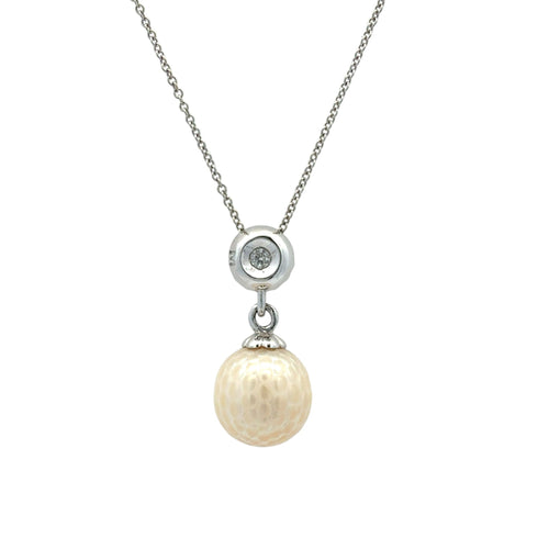 A silver chain necklace featuring a circular silver pendant with a small clear stone, from which hangs a textured, oval cream-colored pearl pendant.