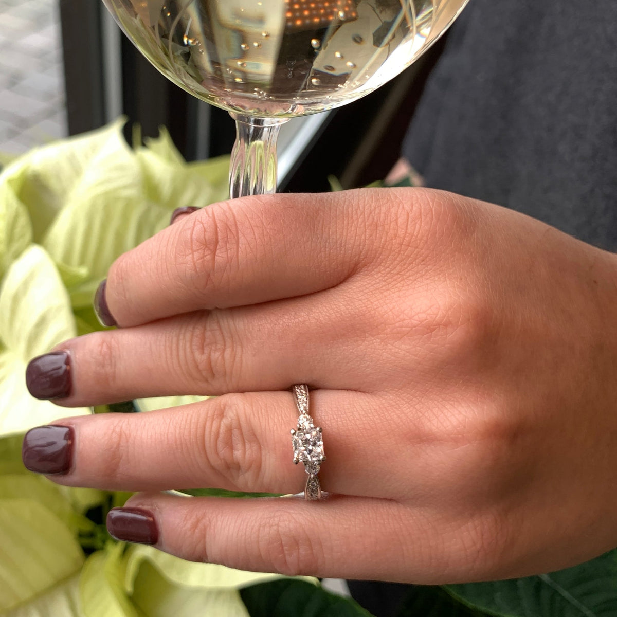 Hand holding a wine glass with a diamond ring on a blurred background