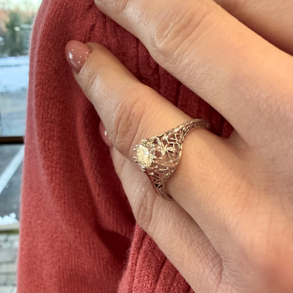 Close-up of a hand wearing a gold ring with intricate design, against a blurred background.