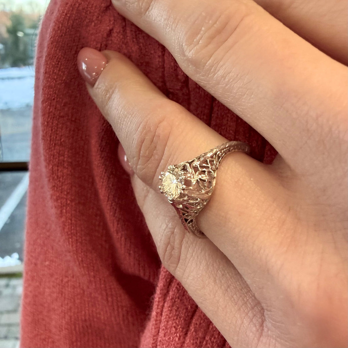 Close-up of a hand wearing a gold ring with intricate design, against a blurred background.