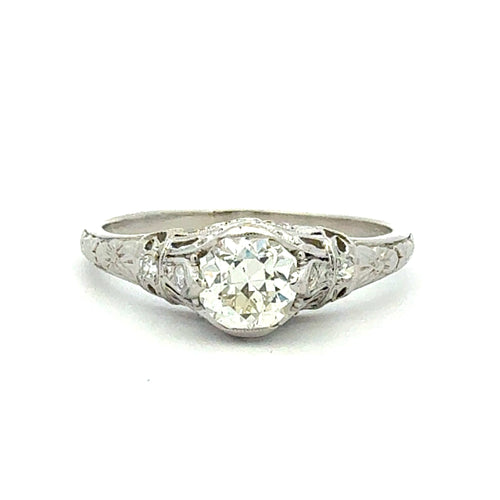 An antique-style diamond ring with a round brilliant-cut center stone and small side diamonds on an ornate silver-toned band, shown on a plain white background.