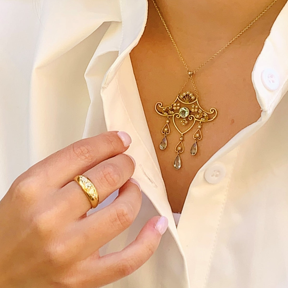 Gold necklace with pendant and ring on a person wearing a white blouse.