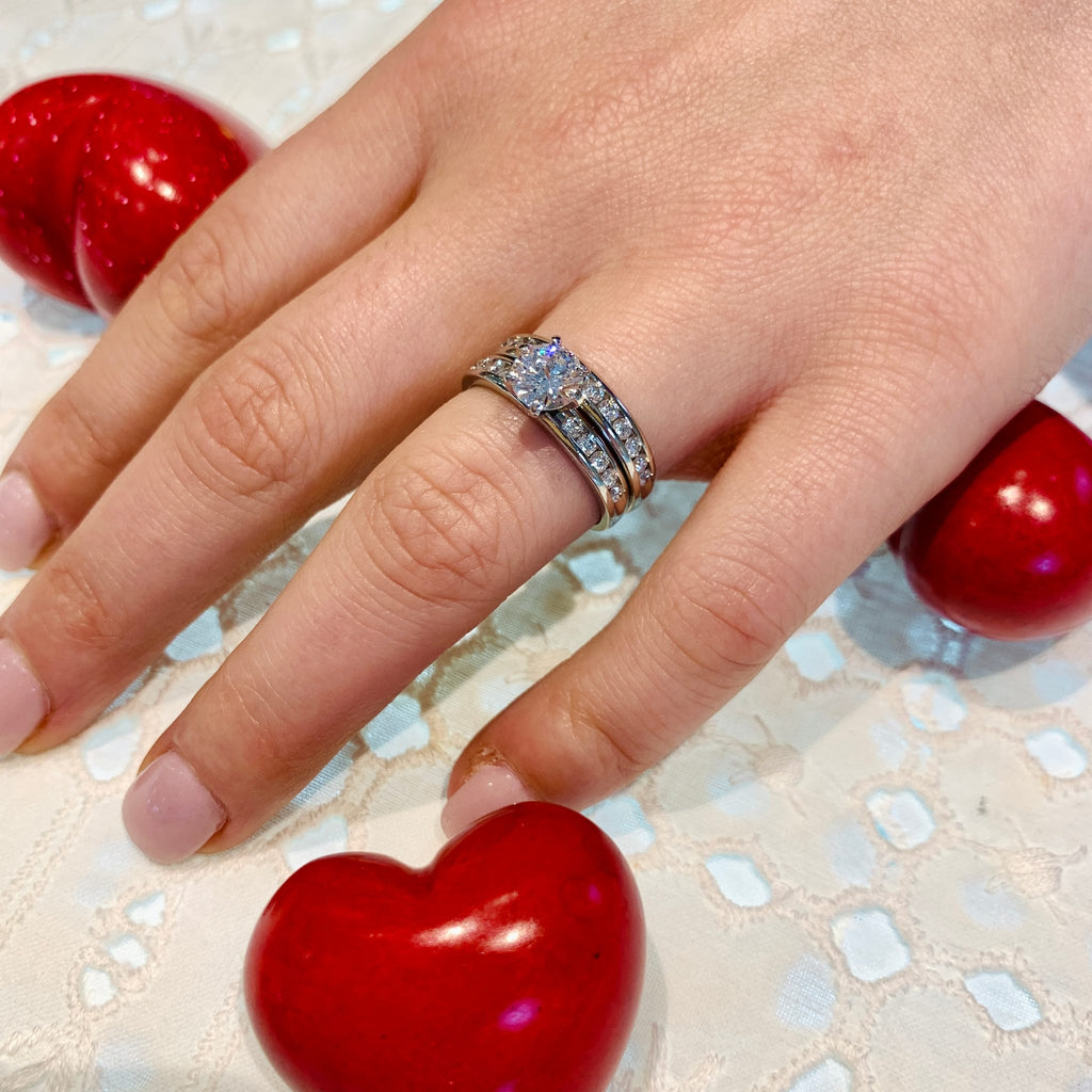 Hand wearing a diamond ring with red heart-shaped objects on a textured surface