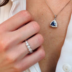 Close-up of a hand wearing a silver ring with a blue gemstone pendant on a chain.