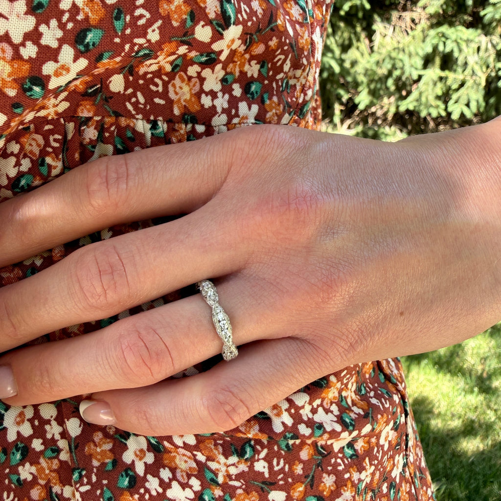 Close-up of a hand wearing a diamond ring with a floral dress and greenery in the background