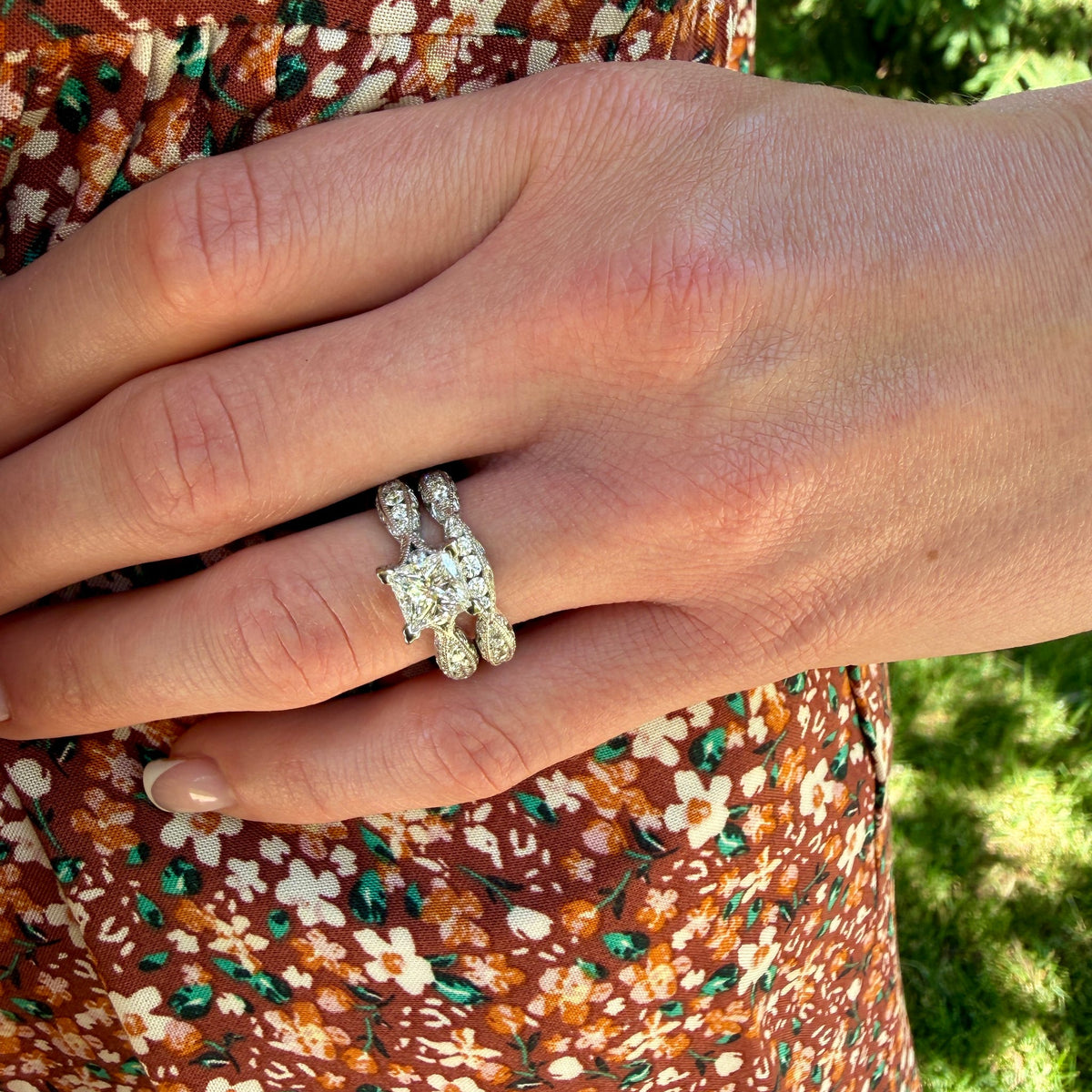 Close-up of a hand wearing a diamond ring with a floral dress and green grass background