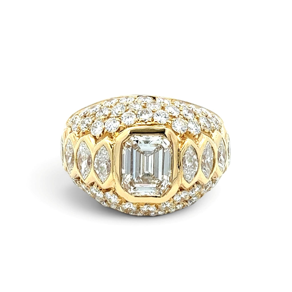 A yellow gold ring featuring a large rectangular emerald-cut center stone surrounded by marquise and round diamonds in a halo setting, with a wider pavé-encrusted top band, shown on a white background.
